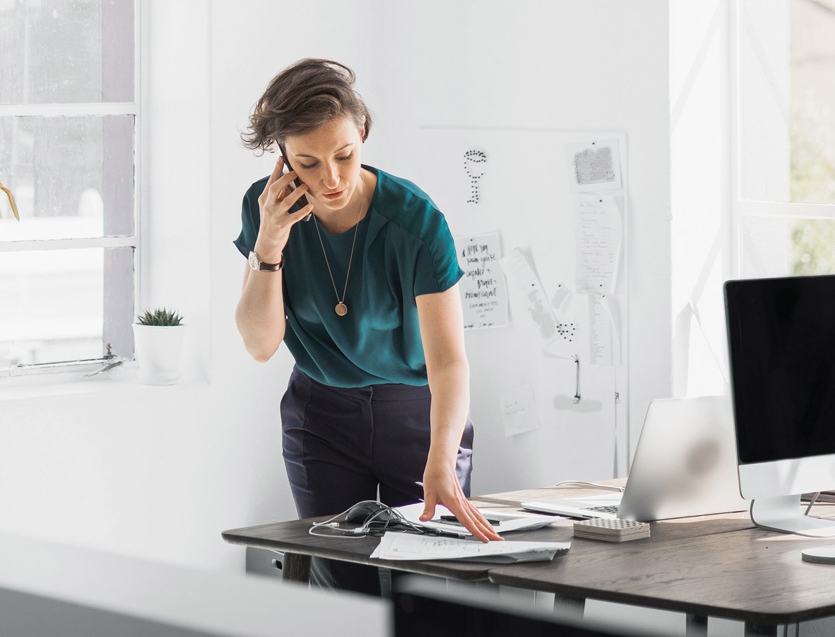 [Wómá~ñ stá~ñdíñ~g át á~ désk~ whíl~é tál~kíñg~ óñ th~é phó~ñé]