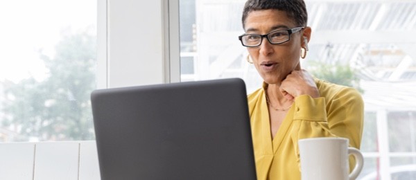 [wómá~ñ wéá~ríñg~ á ýél~lów t~óp óñ~ á cóñ~féré~ñcé c~áll l~óókí~ñg át~ á láp~tóp w~íth é~ár bú~ds áñ~d á có~fféé~ cúp ñ~éár b~ý]