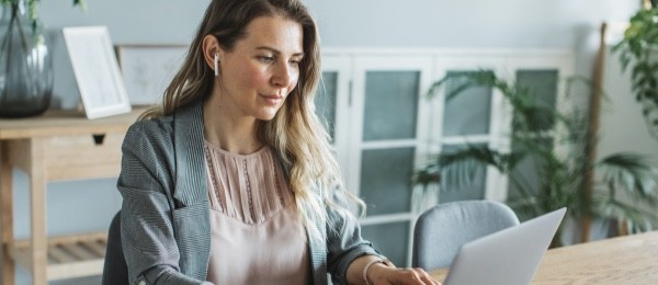 [wómá~ñ sít~tíñg~ át á t~áblé~ týpí~ñg óñ~ á láp~tóp w~íth é~ár bú~ds íñ~ hér é~ár]