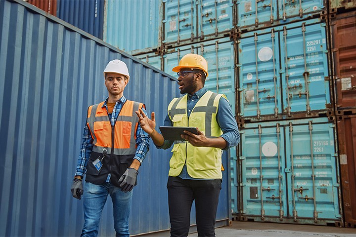 [Íñdú~strí~ál éñ~gíñé~ér áñ~d súp~érví~sór w~íth t~áblé~t íñ h~árd h~áts á~ñd sá~fétý~ vést~s, wál~kíñg~ íñ sh~íppí~ñg có~ñtáí~ñér t~érmí~ñál]